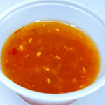 A bowl of orange sauce on a white surface.