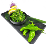 A bowl of green peppers and a slice of lemon on a black plate.