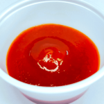 A cup of red sauce on a white surface.